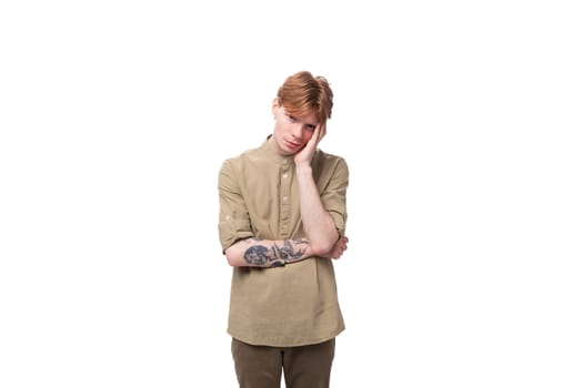 a young european guy with red hair is wearing a fashionable beige shirt and brown trousers feeling tired.