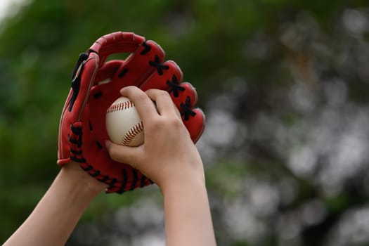 Hand of baseball player in a leather glove holding ball on blurred green background.