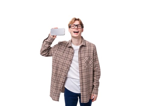 young caucasian guy with red hair in glasses and a plaid shirt shows the screen of a mobile phone with a mockup.