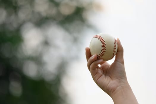 Closeup hand holding a baseball on the sports field. Fitness, sports and training concept.