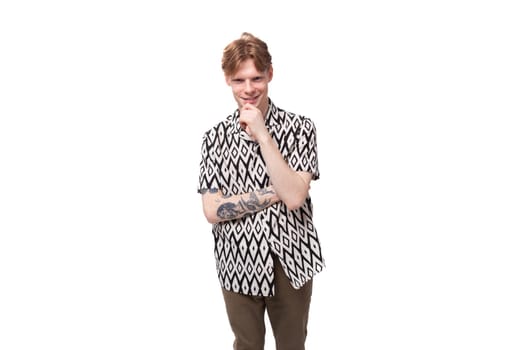 young focused caucasian man with red hair with a tattoo dressed in a summer black and white shirt on a background with copy space.