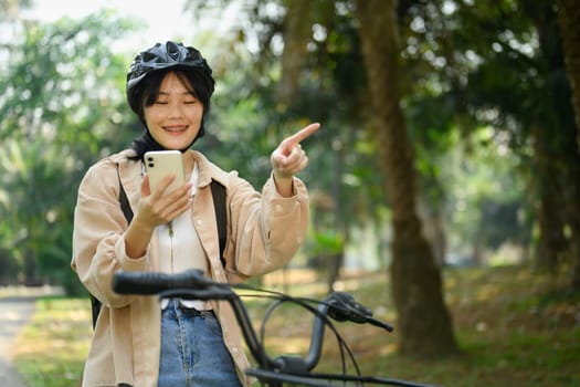 Smiling young woman riding an electric bicycle and using mobile phone for direction.