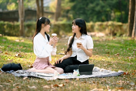 Carefree Asian women friends talking and enjoying coffee in the park after work.