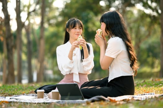 Shot of happy female co workers eating sandwiches on lunch break at outdoors.