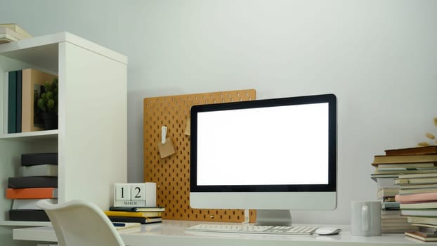 Blank computer desktop, pile of book and pegboard on white table.