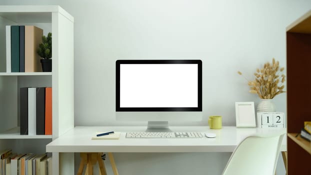 Front view computer display with blank white screen on white table in comfortable home.