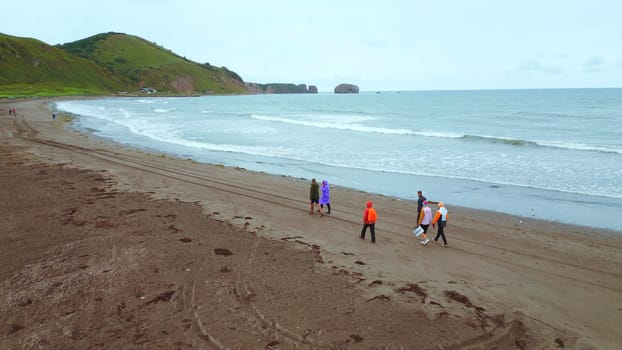 Top view of people by sea with mountain view. Clip. Coast with walking people and amazing mountains on cloudy day. Walk on mountain coast of ocean on cloudy day.