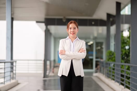 Young happy smiling professional business woman asian, happy confident positive female entrepreneur standing on street arms crossed, looking at camera.