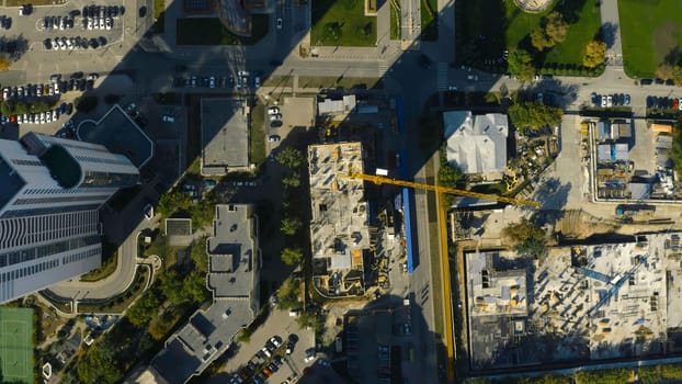 Vertical top view of construction crane in city. Stock footage. Building under construction in center of modern city on sunny summer day. Construction crane in city center.