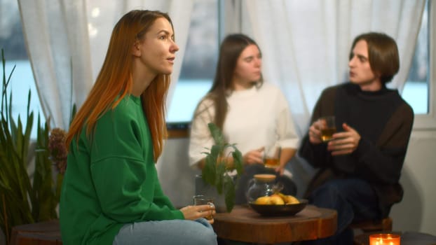Students talk and relax in cozy cafe. Media. Beautiful young woman is drinking tea on background of talking couple. Students relax and drink tea in college cafe.