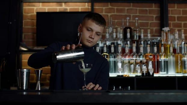 The barman preparing perfect cocktail, standing behind the bar counter. Media. Many bottles of alcohol on the background