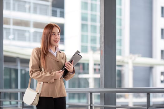 Young beautiful successful business woman outside office building, successful Asian woman smiling standing with documents.