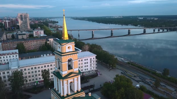 Top view of beautiful city church on river bank with bridge. Clip. Beautiful urban landscape with temple on riverbank on cloudy day. City with church on river with bridge.