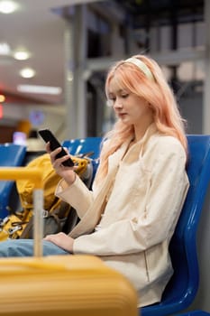 Happy asian tourist woman using mobile smartphone with suitcase traveling between waits for flight in Airport Terminal, flight check in, Tourist journey trip concept.