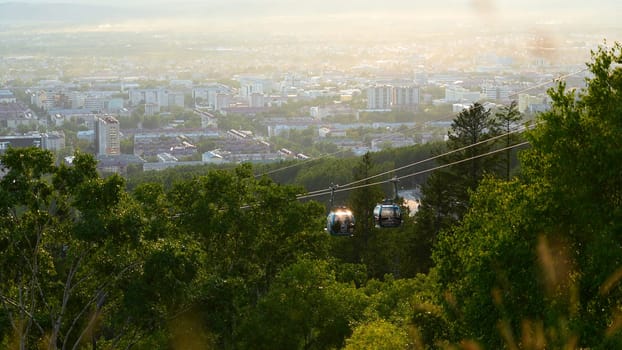 Beautiful view of cable car with view of town in summer. Clip. Green forest on slope with moving cable ways on edge of town. Beautiful city in valley with cable car on sunny summer day.