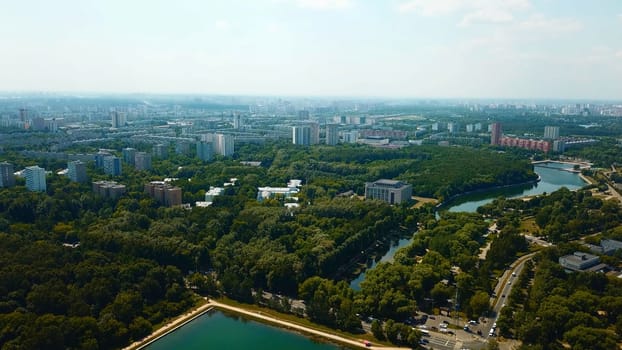 Top view of city with dam and river on sunny summer day. Creative. Beautiful green city with dam and canal on summer day. Skyline of modern city with green parks and clear canal.