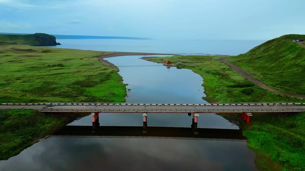 Summer aerial view of the narrow river flowing into the sea. Clip. Concrete bridge crossing calm river