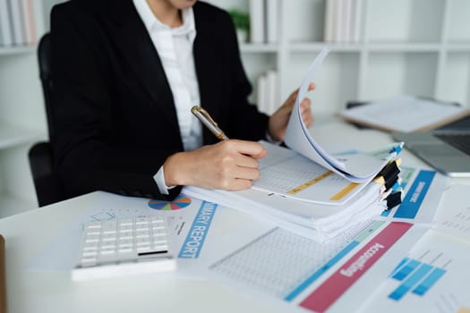 A woman is writing on a piece of paper with a pen. She is wearing a black suit and is sitting at a desk. The paper has a lot of numbers and calculations on it