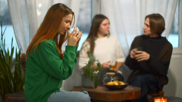 Students talk and relax in cozy cafe. Media. Beautiful young woman is drinking tea on background of talking couple. Students relax and drink tea in college cafe.