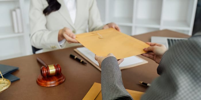 A woman is sitting at a desk with a stack of envelopes in front of her. She is holding the envelopes and she is in a professional setting