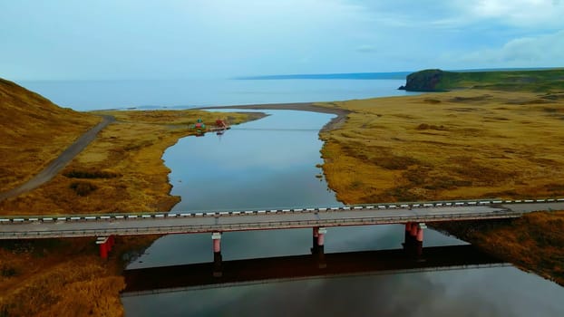 Aerial view of gorgeous nature a bridge between the river shores. Clip. Rural landscape with golden agricultural fields around and the sea shore