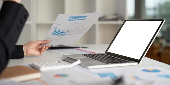 Close up businesswoman using a laptop computer to analysis her financial data. Laptop white screen mockup.