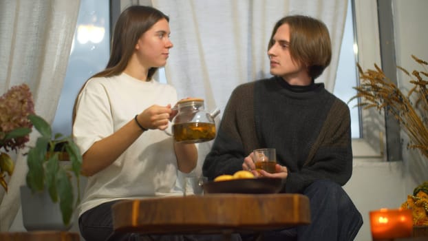 Young man and woman are talking over tea in cafe. Media. Young couple of students are talking with tea in cozy cafe. Couple on student break with tea and comfortable conversation.