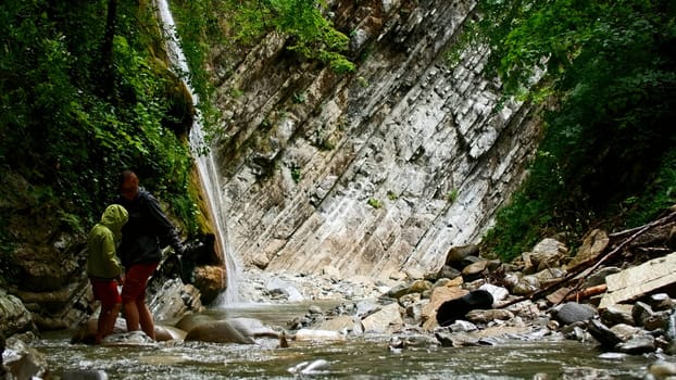 Beautiful waterfall in green forest. Creative. Mother and boy crossing tropical river in mountain jungle