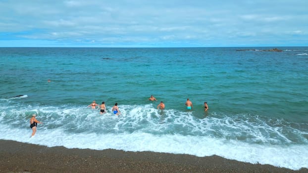 Top view of people swimming in blue water on cloudy day. Clip. Beautiful blue sea with waves and floating people. Tourists swim and relax on beautiful sea with blue water.