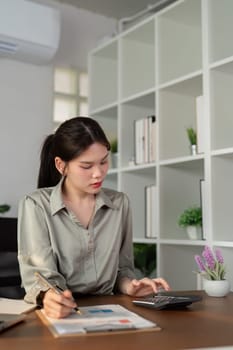 Asian businesswoman using laptop computer and working at office with calculator document on desk, doing planning analyzing the financial report, business plan investment, finance analysis concept.