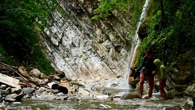 Mother and boy crossing mountain cold water stream with stones. Creative. Hikers in picturesque place