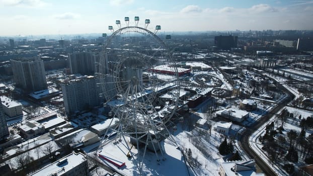 Top view of big Ferris wheel in winter. Creative. Beautiful urban landscape with Ferris wheel in city center in winter. Ferris wheel in center of big city on sunny winter day.