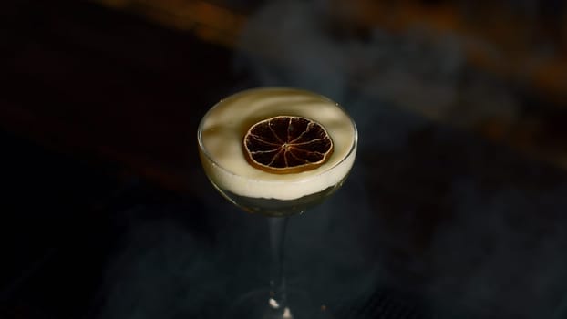 Close up of beautiful cocktail with thick foam and dried orange slice. Media. Beverage on bar counter background