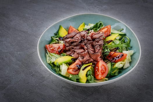 Tasty salad - roasted veal loin, avocado, boiled eggs and fresh vegetables on stone table