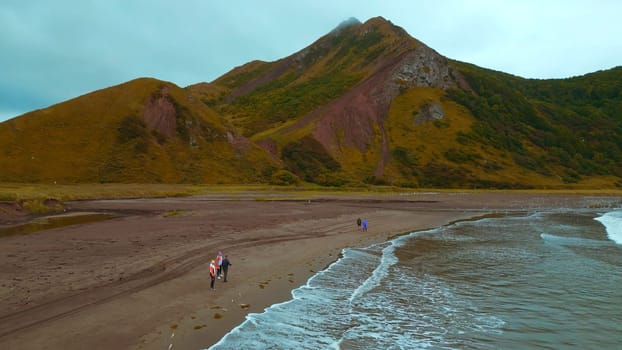 Top view of people by sea with mountain view. Clip. Coast with walking people and amazing mountains on cloudy day. Walk on mountain coast of ocean on cloudy day.