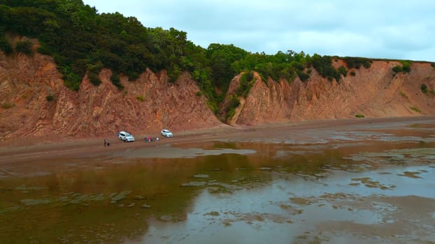 Top view of coast with tourists and rocky gorge. Clip. Amazing coast with rocks and tourists at gorge. Forest gorge on shore of rocky cliff with tourists.