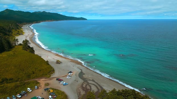 Top view of green forest on coast with tourists and turquoise water. Clip. Amazing landscape with green forest on coast with turquoise sea. Tourists relax on shore of mountain coast of ocean.