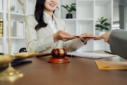 A woman is sitting at a desk with a stack of envelopes in front of her. She is holding the envelopes and she is in a professional setting