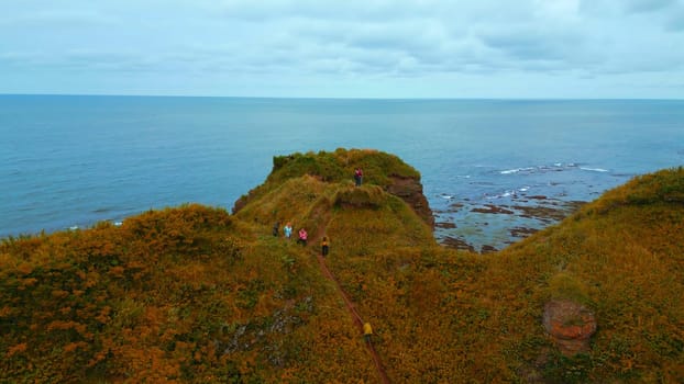 Top view of beautiful seascape with tourists on rock. Clip. Inspiring approach to edge of rocky coast. Beautiful view of tourists on cliff overlooking sea horizon.