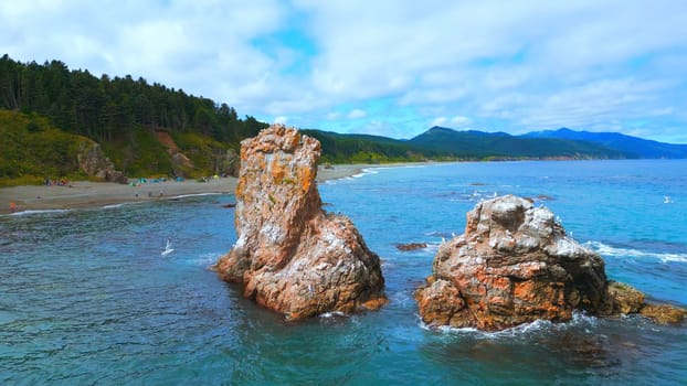 Top view of rocks in sea and coast with tourists. Clip. Beautiful coast with rocks and turquoise water. Camping vacation on wild coast of sea with rocks.