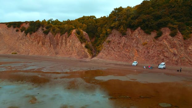 Top view of coast with tourists and rocky gorge. Clip. Amazing coast with rocks and tourists at gorge. Forest gorge on shore of rocky cliff with tourists.