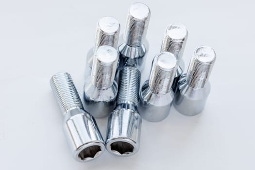 shiny steel chrome coated wheel bolts on white background, full-frame closeup high angle view, real photo