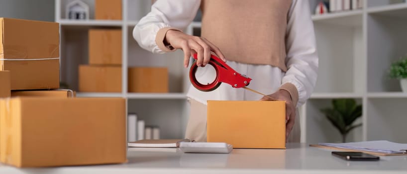 Woman asian use scotch tape to attach parcel boxes to prepare goods for the process of packaging, shipping, online sale internet marketing ecommerce concept startup business idea.