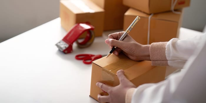 Woman is writing a list of customer on paper before shipping to them, she runs an ecommerce business on websites and social media. Concept of selling products online.