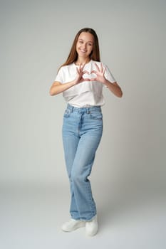 Smiling young woman showing heart sign with hands on gray background close up