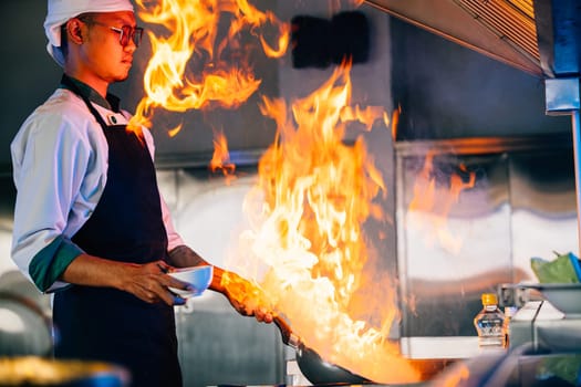 In professional kitchen chef hands handle flaming wok. Closeup of cooking expertise flames at work. Skillful chef burning food working in a modern kitchen setting. cook food with fire