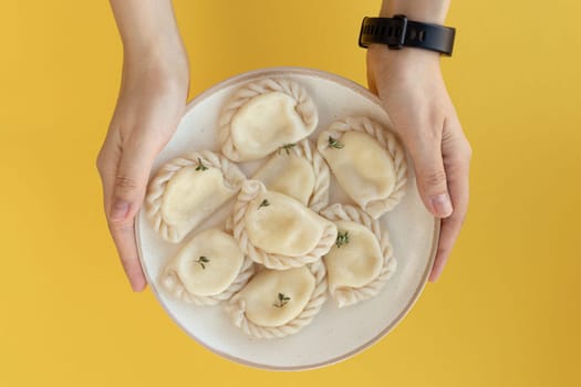 flat lay on female hands holding a plate of ravioli or dumplings. top view of plate on yellow background