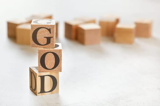 Three wooden cubes with word GOD, on white table, more in background, space for text in right down corner