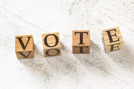 Four wooden cubes with word VOTE on white working board.