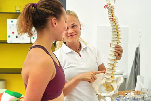 Young woman patient at physiotherapy consultation, physiotherapist explaining back bones on spine model